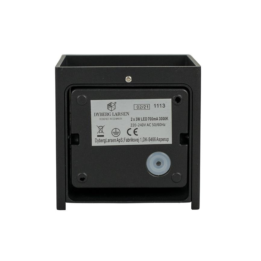 Eine quadratische schwarze LED-Leuchte zeigt ihre Rückseite; Etikett, Schrauben und eine runde Gummikabelverschraubung sind auf einem einheitlichen weißen Hintergrund sichtbar.
 
 Text auf dem Etikett:
 DYBERG LARSEN
 DESIGNED IN DENMARK
 02/21 1113
 2 x 3W LED 700mA 3000K
 220–240 V Wechselstrom, 50/60 Hz
 DybergLarsen ApS, Fabriksvej 1, DK-5466 Asperup