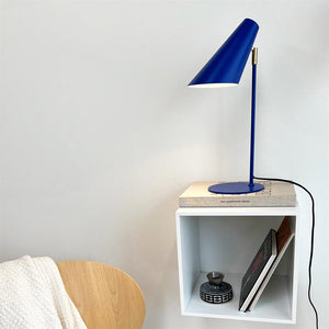 Blaue Lampe scheint auf ein Buch, das auf einem weißen Wandregal steht; Auf dem Regal stehen eine kleine Keramikschale und Bücher, daneben ein Holzstuhl mit weißem Teppich.
 Text zum Buch: „new scandinavian design“