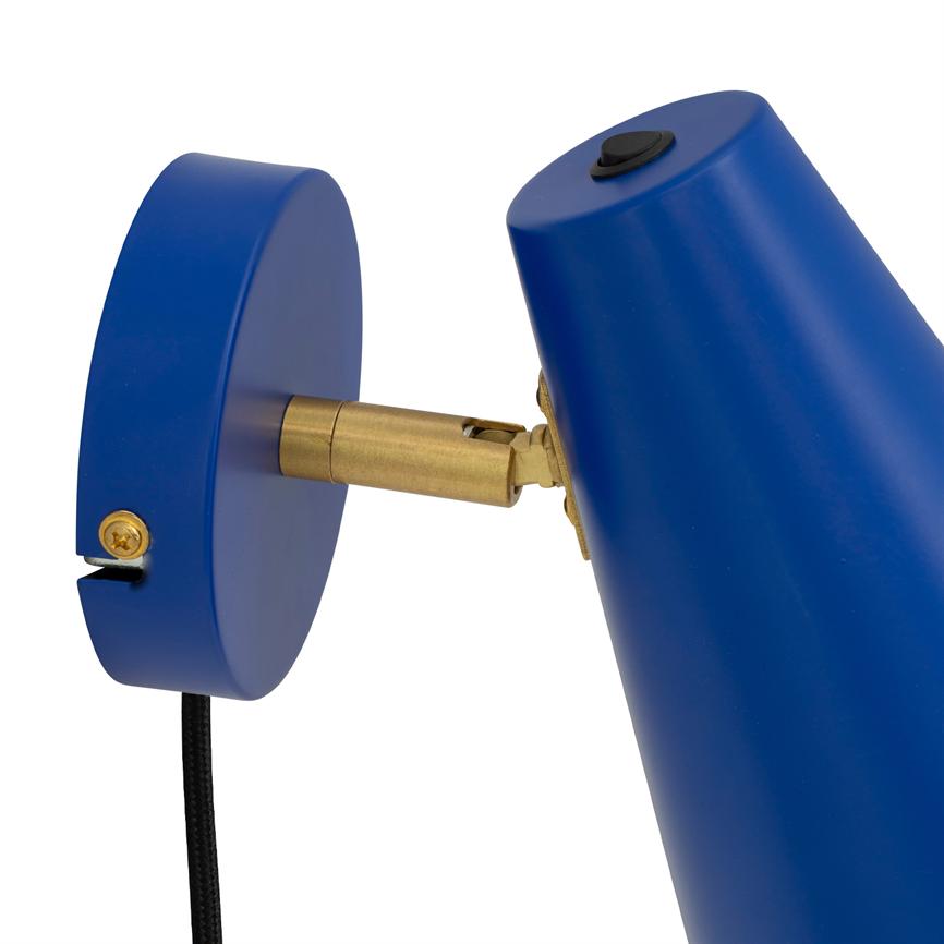 Die blaue Wandleuchte wird über ein Messinggelenk abgewinkelt und an einer runden Wandplatte befestigt. Vor einem weißen Hintergrund hängt eine schwarze Stoffschnur herab.