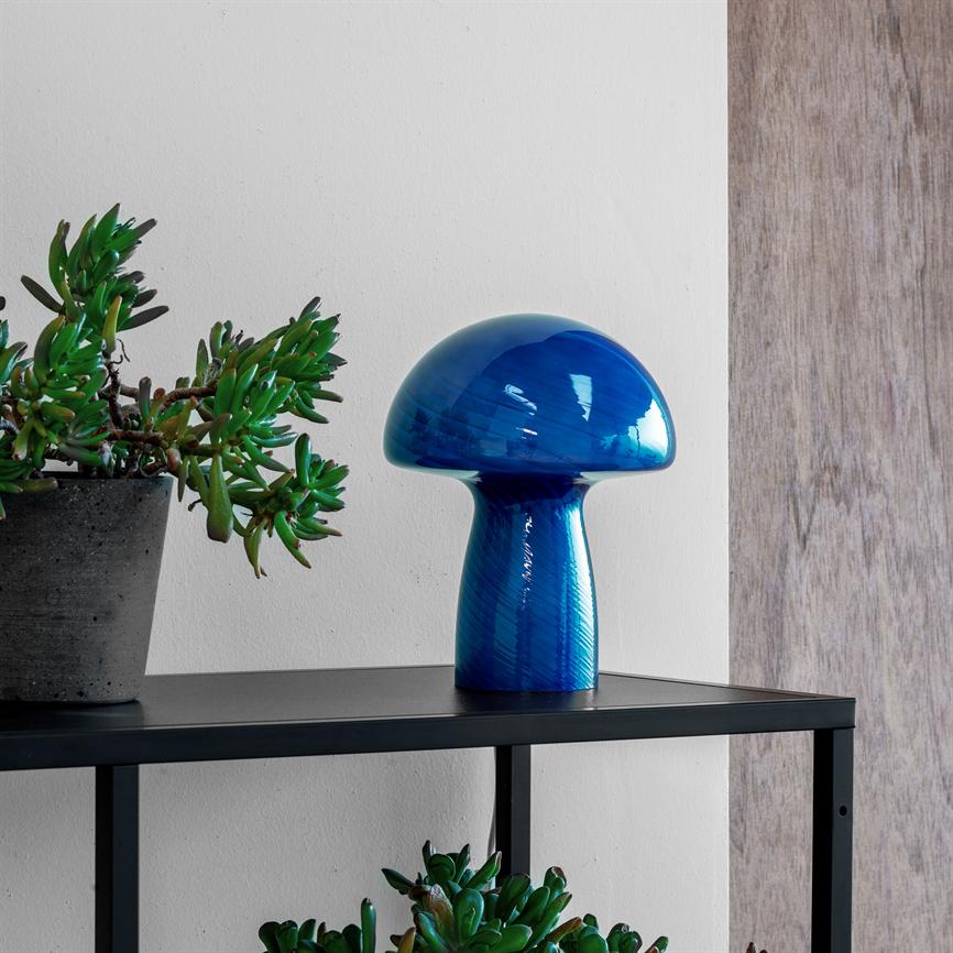 Blaues, pilzförmiges Glasobjekt steht auf einem schwarzen Metallregal neben einem grauen Topf mit Sukkulenten; Weiße Wand dahinter und helle Holzvertäfelung rechts.