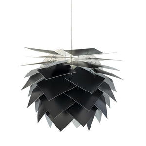 Pendellampe med overlappende matte sorte plader, hænger fra en tynd ledning mod en ensartet hvid baggrund og ligner en stor arkitektonisk kogle.