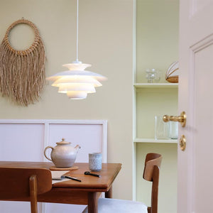 Ein Weißes pendel Lichter über einem Holztisch mit Teekanne und Tasse in einer hellen Wohnküche, umgeben von einem Wandbehang aus Korbgeflecht, eingebauten Regalen und einer offenen Tür mit Messinggriffen.