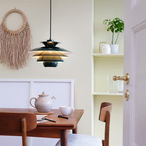 Eine Pendelleuchte hängt über einem Holztisch und spendet warmes Licht. Eine Teekanne, eine Tasse, ein Notizbuch und ein Stift stehen auf dem Tisch in einer gemütlichen Essecke mit Makramee, Regal und offener Tür.