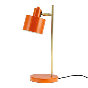 Eine orangefarbene Tischlampe aus Metall neigt sich mit ihrem zylindrischen Schirm nach unten; Es steht auf einem runden orangefarbenen Sockel mit einem schlanken Messingstab und einer schwarzen Kordel vor einem weißen Hintergrund.