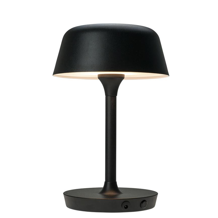 Tischleuchte mit rundem, schwarzem Schirm auf schlankem Schaft: strahlt weiches, nach unten gerichtetes Licht über einen runden Sockel ab, vor einem klaren, weißen Hintergrund.