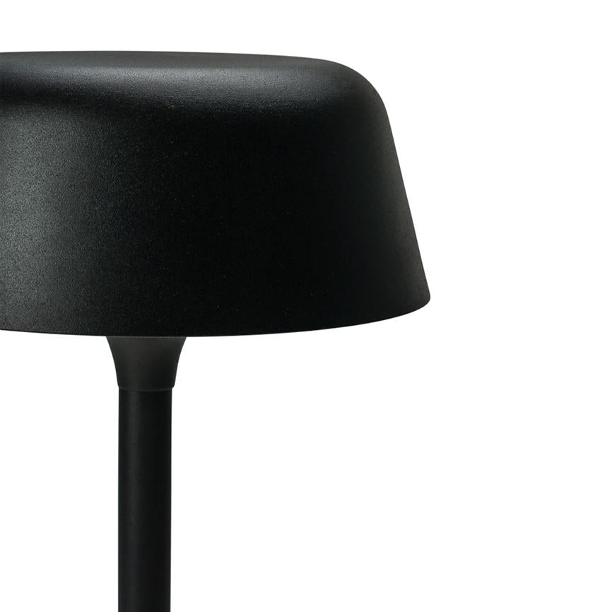 Schwarze Tischleuchte steht mit gewölbtem Schirm auf einem schlanken Stab; teilweise nach rechts beschnitten vor einem reinweißen Hintergrund.