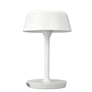 Eine weiße Tischlampe steht aufrecht; der Schirm ist leicht nach außen gebogen und auf einem schlanken Stab und einem runden Sockel montiert; neutralweißer Hintergrund ohne andere Objekte.