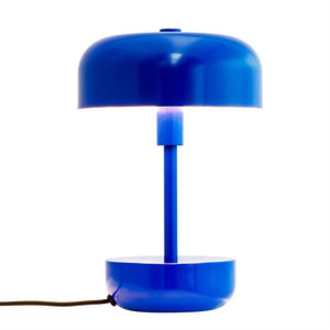 Blaue, runde Tischlampe leuchtet schwach zwischen Bildschirm und Säule; Der zylindrische Stab verbindet die obere und untere Schüssel, vor weißem Hintergrund, mit schwarzer Stoffschnur nach links.