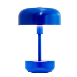 Eine blaue Tischlampe mit rundem Schirm und Sockel strahlt weißes Licht durch den Raum zwischen Schirm und Sockel ab und steht vor einem sauberen, weißen Hintergrund.