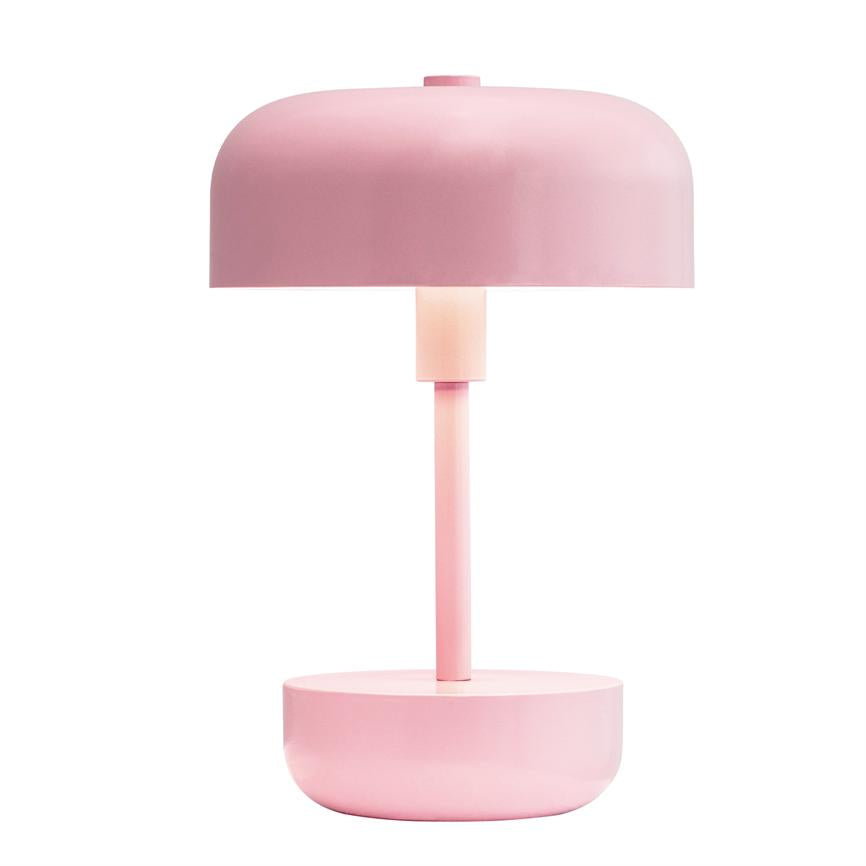 Die Lampe steht auf einem runden Sockel und strahlt sanftes, nach unten gerichtetes Licht durch eine mattrosa Kuppel ab; minimalistisches Design vor weißem Hintergrund.