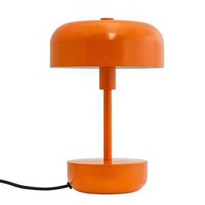 Auf weißem Hintergrund steht eine orangefarbene Tischleuchte aus Metall: runde Kuppel, schmale Säule, zylindrischer Sockel und runder Fuß, nach links verläuft das schwarze Netzkabel.