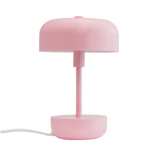 Eine mattrosa Tischlampe steht aufrecht; runder Schirm über einem schmalen Mast und rundem Sockel, vor einem einheitlichen weißen Hintergrund.