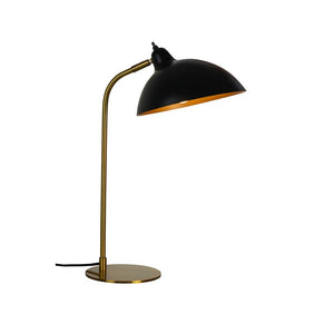 Eine Schreibtischlampe mit schwarzem Kuppelschirm und goldenem Innenleben, die nach unten geneigt ist und Licht spendet; schlanker goldener Ständer und flacher runder Sockel auf weißem, neutralem Hintergrund.