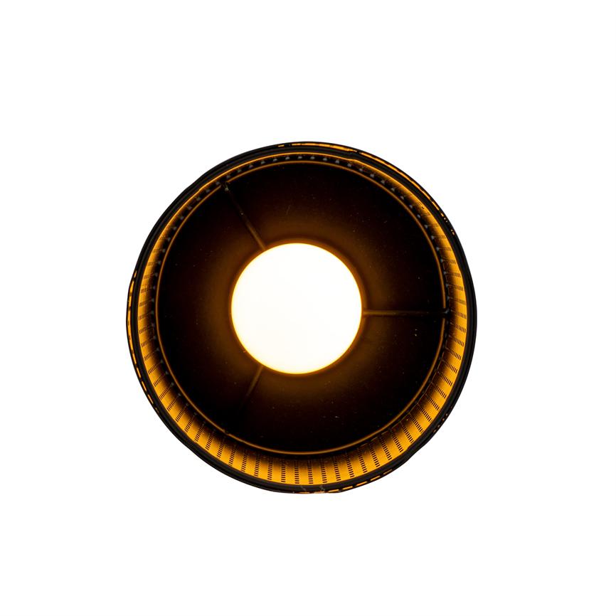 Eine runde Deckenleuchte strahlt aus der Mitte intensives warmes Licht aus, umgeben von einem dunklen, perforierten Innenschirm, der einen goldenen Glanz auf einen weißen Hintergrund wirft.