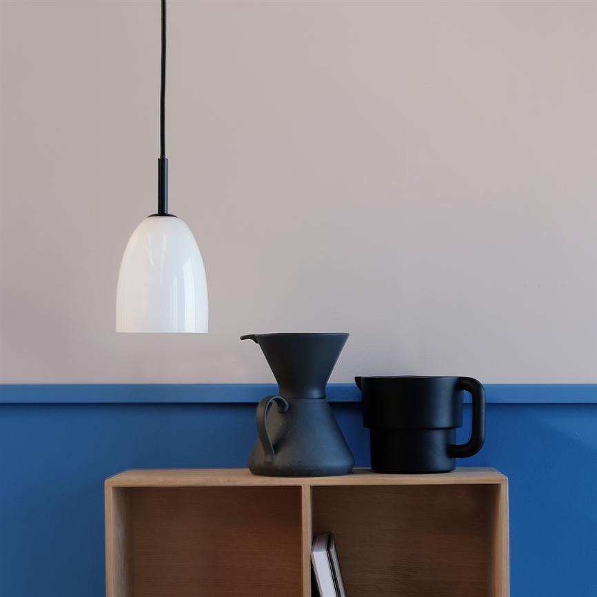 Ein Weißes pendel hängt und wirft sanftes Licht über ein Holzregal; Zwei mattschwarze Krüge stehen im Regal vor einer hellgrauen Wand mit blauem Wandpaneel.