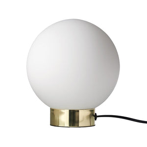 En hvid kuglelampe står på en blank messingfod; en sort ledning løber ud mod en neutral hvid baggrund.