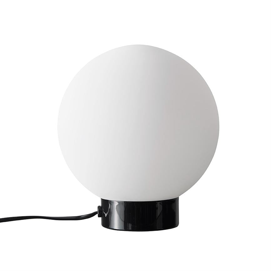 Kugellampe: Eine große weiße Glaskugel sitzt auf einem glänzend schwarzen zylindrischen Sockel, an dessen Seite ein schwarzes Kabel ausläuft, vor einem neutralweißen Hintergrund.