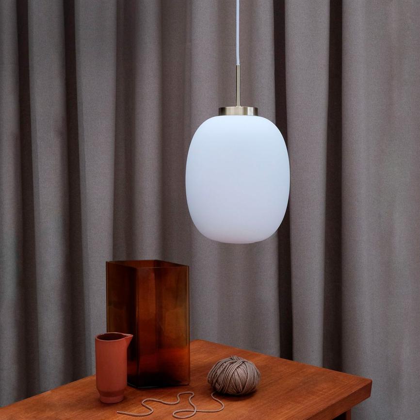 Ein weißes Oval pendel hängt über einem Holztisch; Auf dem Tisch stehen eine hohe braune Glasvase, eine kleine Terrakotta-Tasse und ein Bindfadenschlüssel mit loser Schnur. Der Hintergrund sind graue Vorhänge.