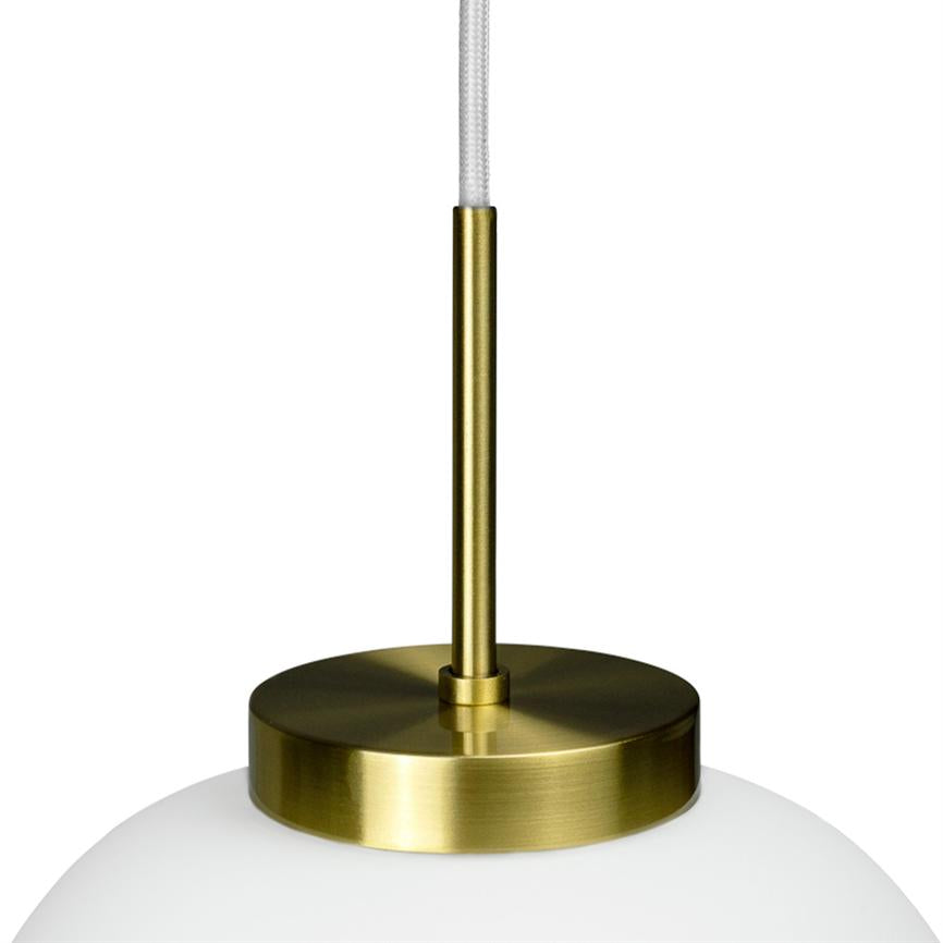 Pendelleuchte hängt an einer weißen Textilschnur; Ein schlanker Messingstab verbindet eine runde Messingplatte mit einer milchig weißen Glaskuppel auf einem schlichten weißen Hintergrund.