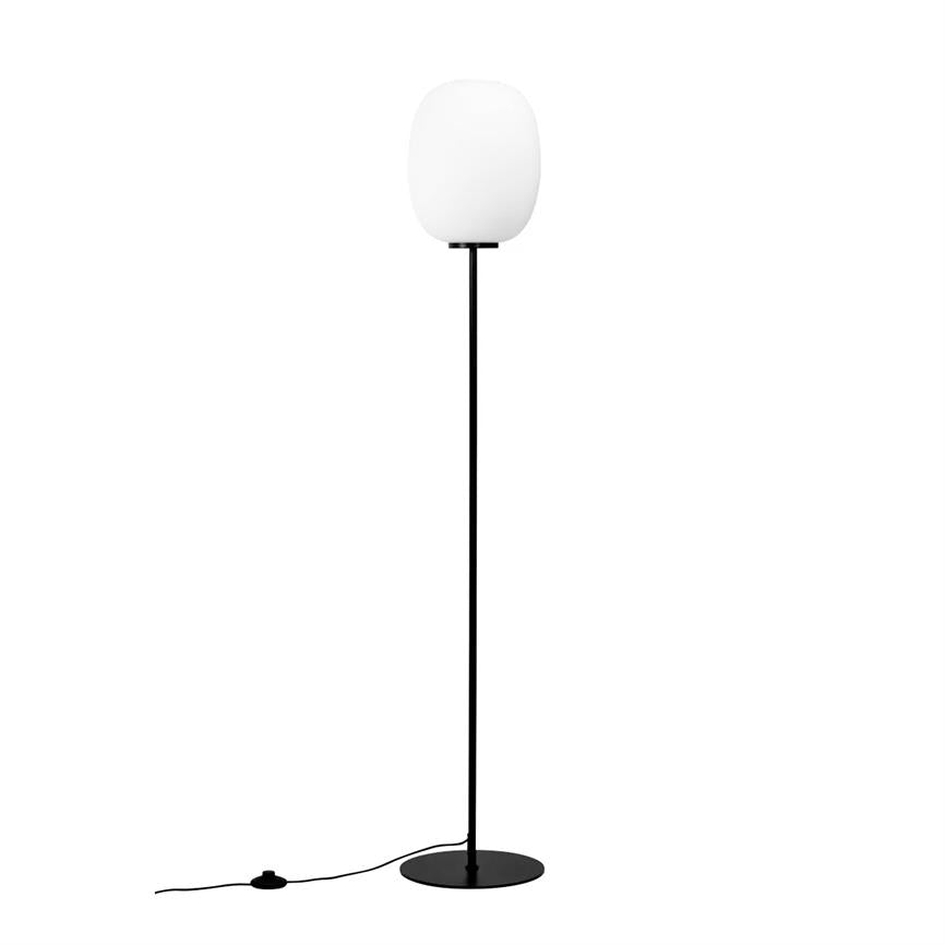 Gulvlampe med hvid oval skærm står oprejst; tynd sort stang og rund sort fod, synlig sort ledning med fodkontakt, placeret mod en ensartet hvid baggrund.