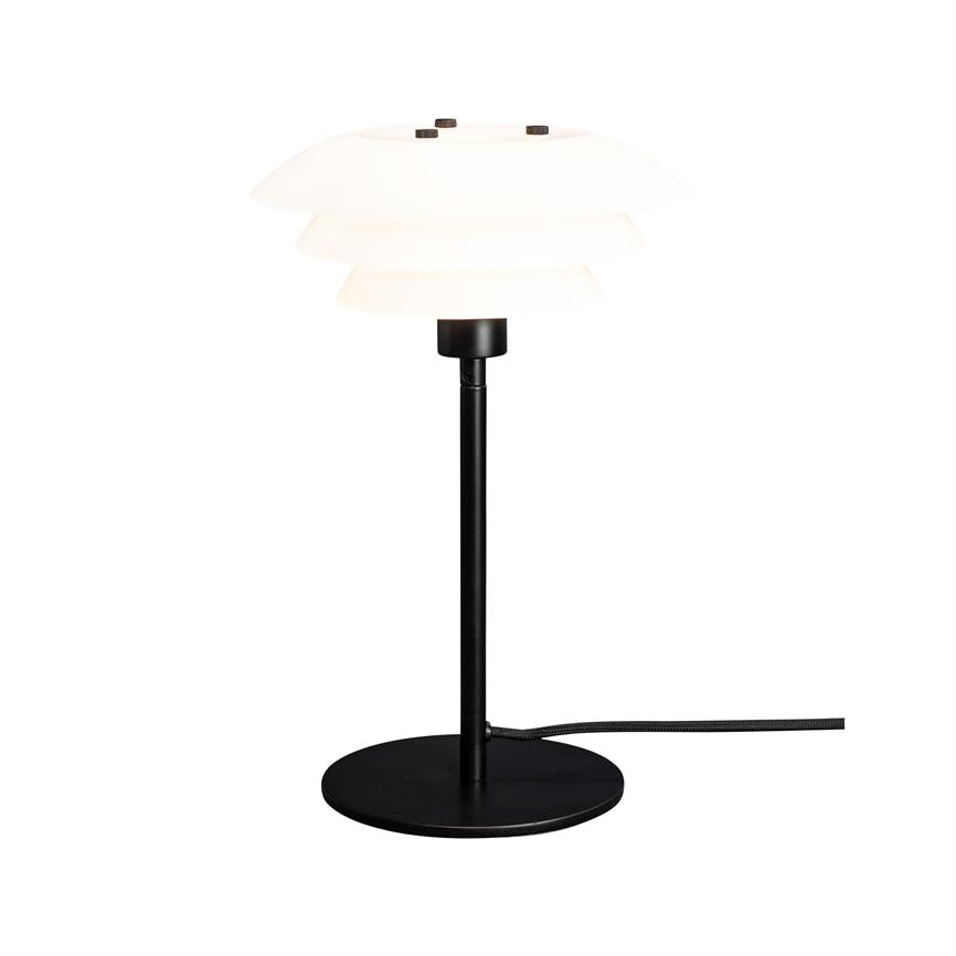 Tischlampe mit geschichtetem weißem Schirm, der sanftes Licht ausstrahlt; Schlanker schwarzer Metallstab und runder schwarzer Fuß mit sichtbarer, mit Stoff überzogener Kordel, vor einem weißen Hintergrund.