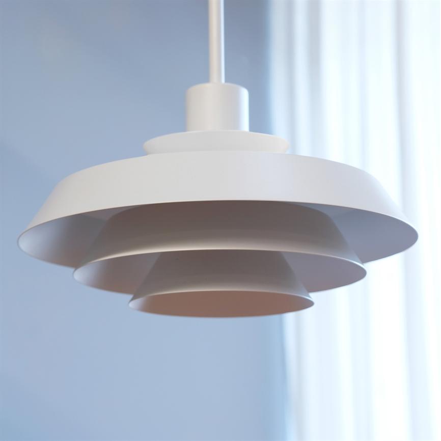 Eine weiße, abgestufte Pendelleuchte hängt ruhig von der Decke; seine kreisförmigen Bildschirme überlappen sich. Der Hintergrund zeigt eine sanftblaue Wand und helle, durchscheinende weiße Vorhänge.