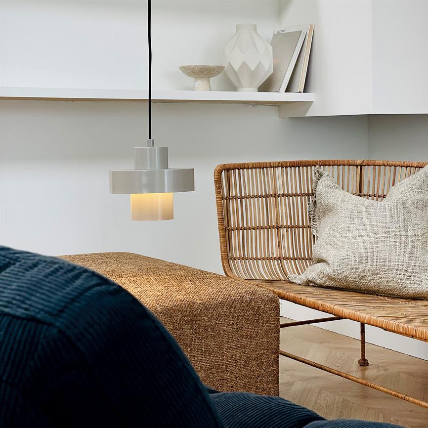 In einer hellen, minimalistischen Ecke mit Rattanbank, naturfarbenen Kissen und einem schlichten Regal mit Keramikvasen strahlt eine mattgraue Hängelampe warm nach unten.