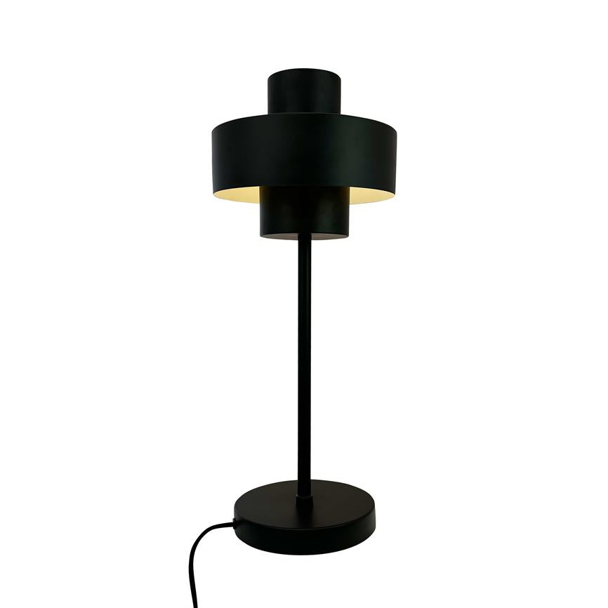 Eine schwarze Tischlampe mit überlappenden zylindrischen Schirmen strahlt warmes, nach unten gerichtetes Licht aus; es steht auf einem runden Sockel mit sichtbarem Draht vor einem einheitlichen weißen Hintergrund.