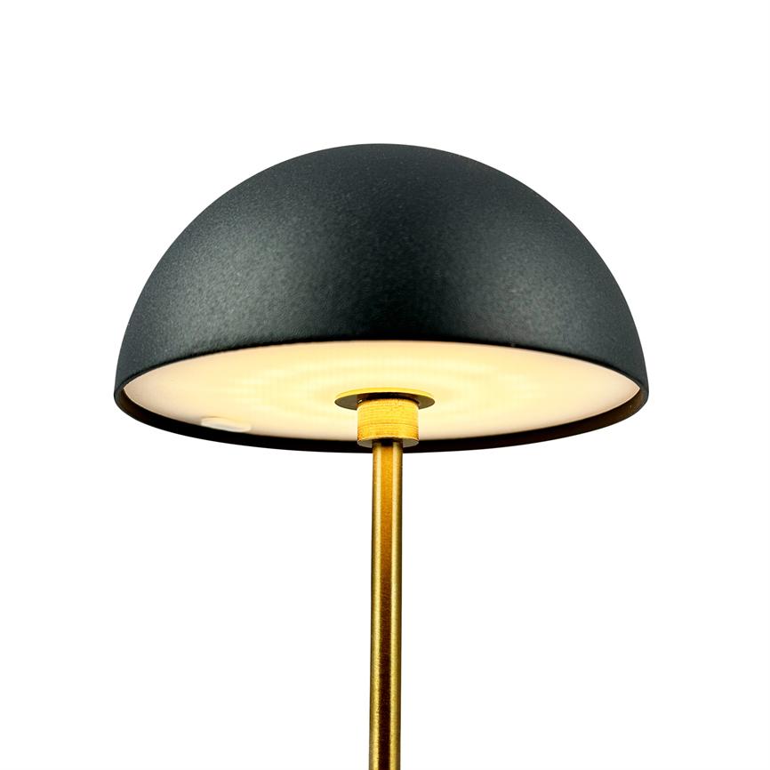 Lampe med sort kuppelskærm på gylden stang udsender varmt, blødt lys under skærmens hvide underside; minimalistisk, moderne design mod en neutral hvid baggrund.