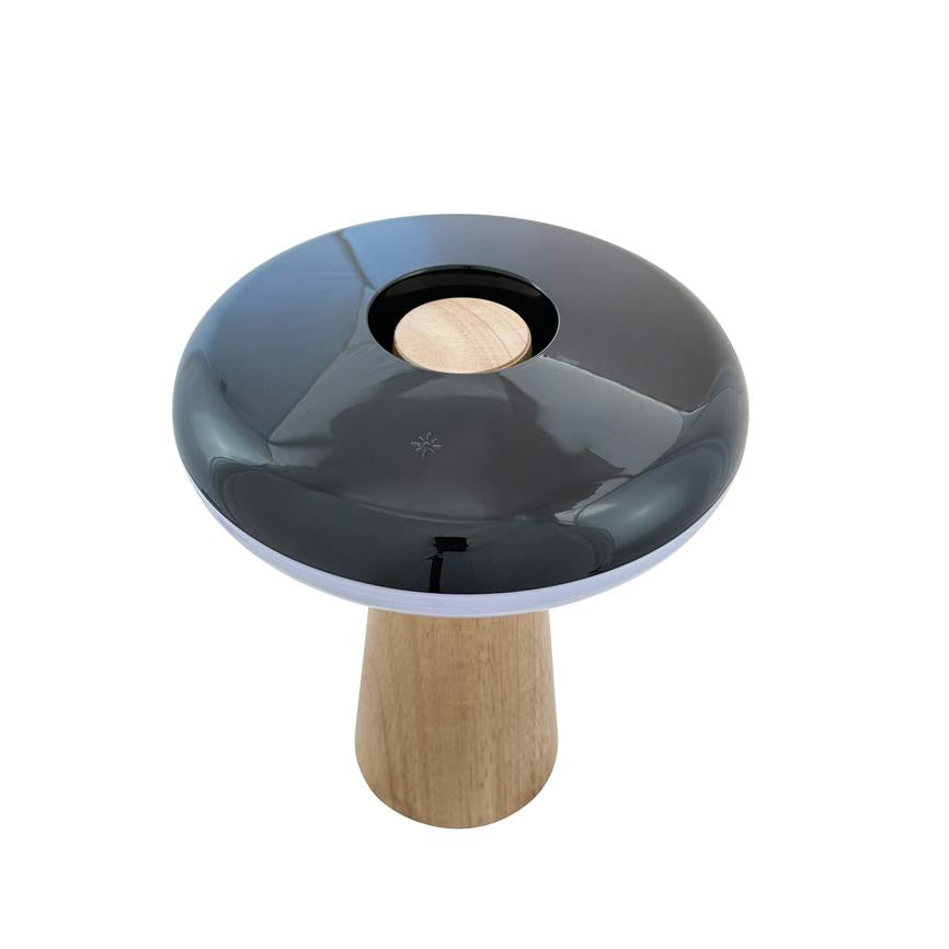 Tischlampe mit pilzartiger Form, glänzend schwarzer Oberseite mit zentraler runder Kerbe und hellem Holzsockel; Produktfoto auf weißem Hintergrund im hellen Studio.