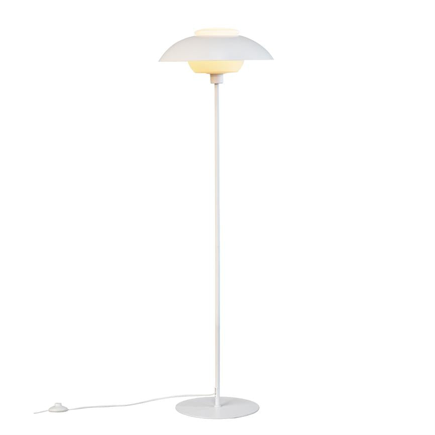 Weiße Stehlampe ist eingeschaltet; Runder Schirm spendet warmes Licht, schmaler Stab verbindet Schirm mit rundem Fuß, Netzkabel mit Fußschalter liegt ausgestreckt auf weißem Hintergrund.