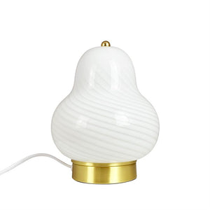 Weiße birnenförmige Tischlampe mit gewellter, gerillter Glasoberfläche, mit kleinem Goldknopf oben, auf rundem Messingsockel platziert; Elektrokabel verläuft nach links vor einem einheitlichen weißen Hintergrund.