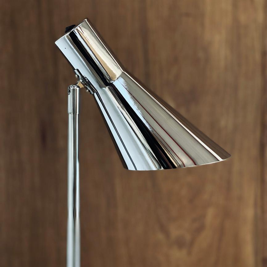 Eine verchromte Leselampe beugt ihren konischen Schirm nach unten und reflektiert die Umgebung, montiert auf einem schlanken Mast vor einem warmen, holzverkleideten Hintergrund.