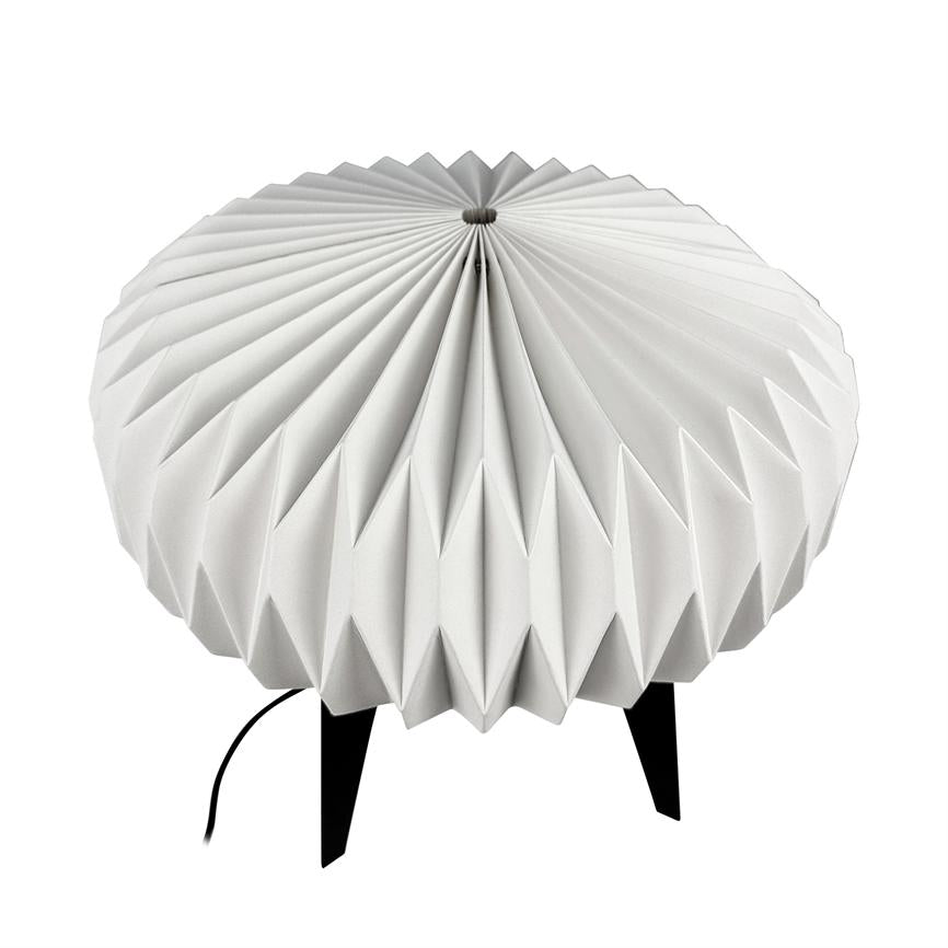 Runde Lampe mit plissiertem weißen Schirm ruht auf drei schwarzen Beinen; Auf einem reinweißen Hintergrund ist ein schwarzes Stromkabel zu sehen, das vom unteren Bildschirmrand verläuft.