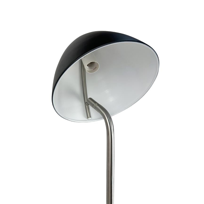 Gulvlampe med sort yderside og hvid inderside; skærm vinklet opad, pærefatning synlig; buet rustfri stålstang mod ensartet hvid baggrund.