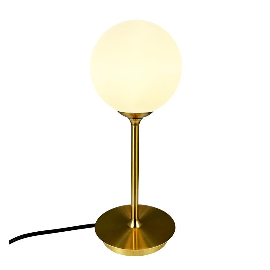 Bordlampe med opal hvid kugleskærm, som udsender varmt lys, monteret på slank messingstang og cirkulær messingfod; sort strømkabel ligger skråt mod venstre på hvid baggrund.