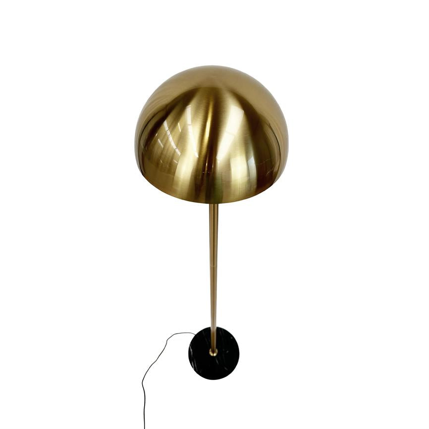 Gulvlampe med blank, messingfarvet halvkugleskærm står på en slank stang over en sort rund marmorbase; sort ledning ligger løst ved siden af, mod en ensartet hvid baggrund.
