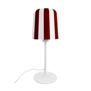 Bordlampe står oprejst; lampeskærm med brede, lodrette røde og hvide striber; tynd hvid stander og rund base; hvid ledning slanger let ud mod venstre på ensartet hvid baggrund.