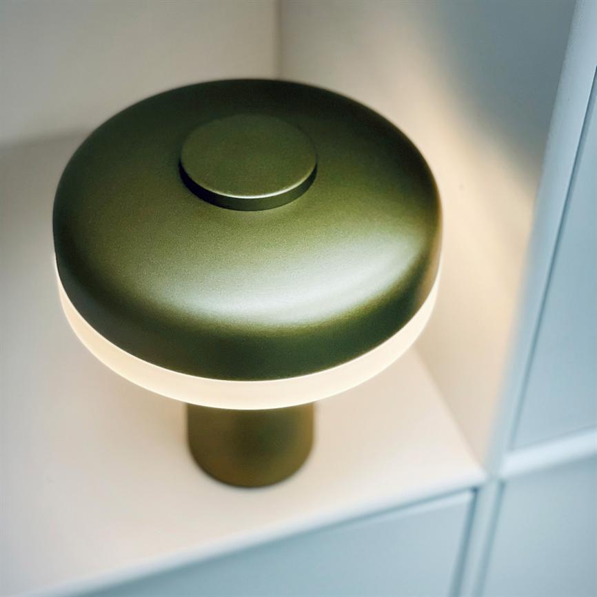 Eine grüne, pilzförmige Tischlampe mit mattem Finish strahlt weiches, warmes Licht aus; es steht auf einem weißen Regal in einem modularen Regalsystem.
