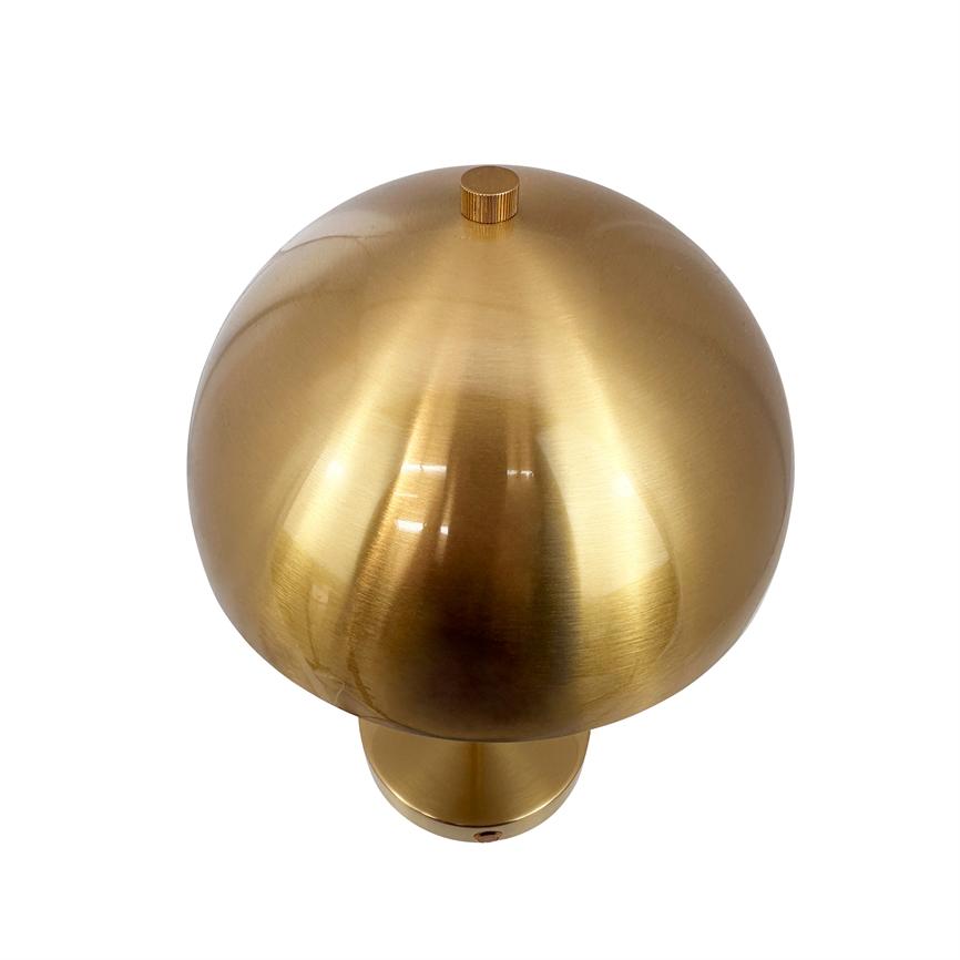 Kugleformet messinglampe med børstet, reflekterende overflade hviler på en kort cylindrisk sokkel foran en ensfarvet hvid baggrund.