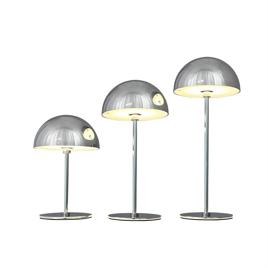Drei chromfarbene halbkugelförmige Tischlampen leuchten; Sie stehen in drei verschiedenen Höhen nebeneinander auf einem einheitlichen weißen Hintergrund.