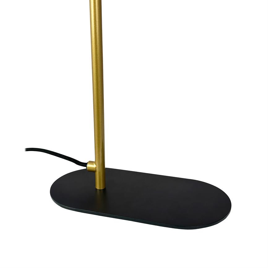 Gylden lampestang står i oval sort fod; sort stofledning løber ud fra siden. Minimalistisk bordlampe på ensartet hvid baggrund.