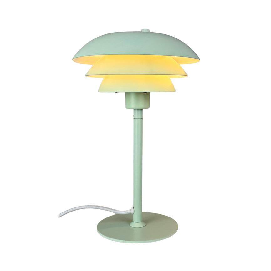 Bordlampe i mintgrøn metal med flerlags, skålformet skærm, udsender varmt diffust lys; slank stander på rund fod og hvid tekstilledning, placeret mod neutral hvid baggrund.